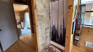 Ein Holzblockhaus-Interieur mit einer Steinwand, einer Duschvorhangs mit Waldmotiv und einem Fenster mit Aussicht.