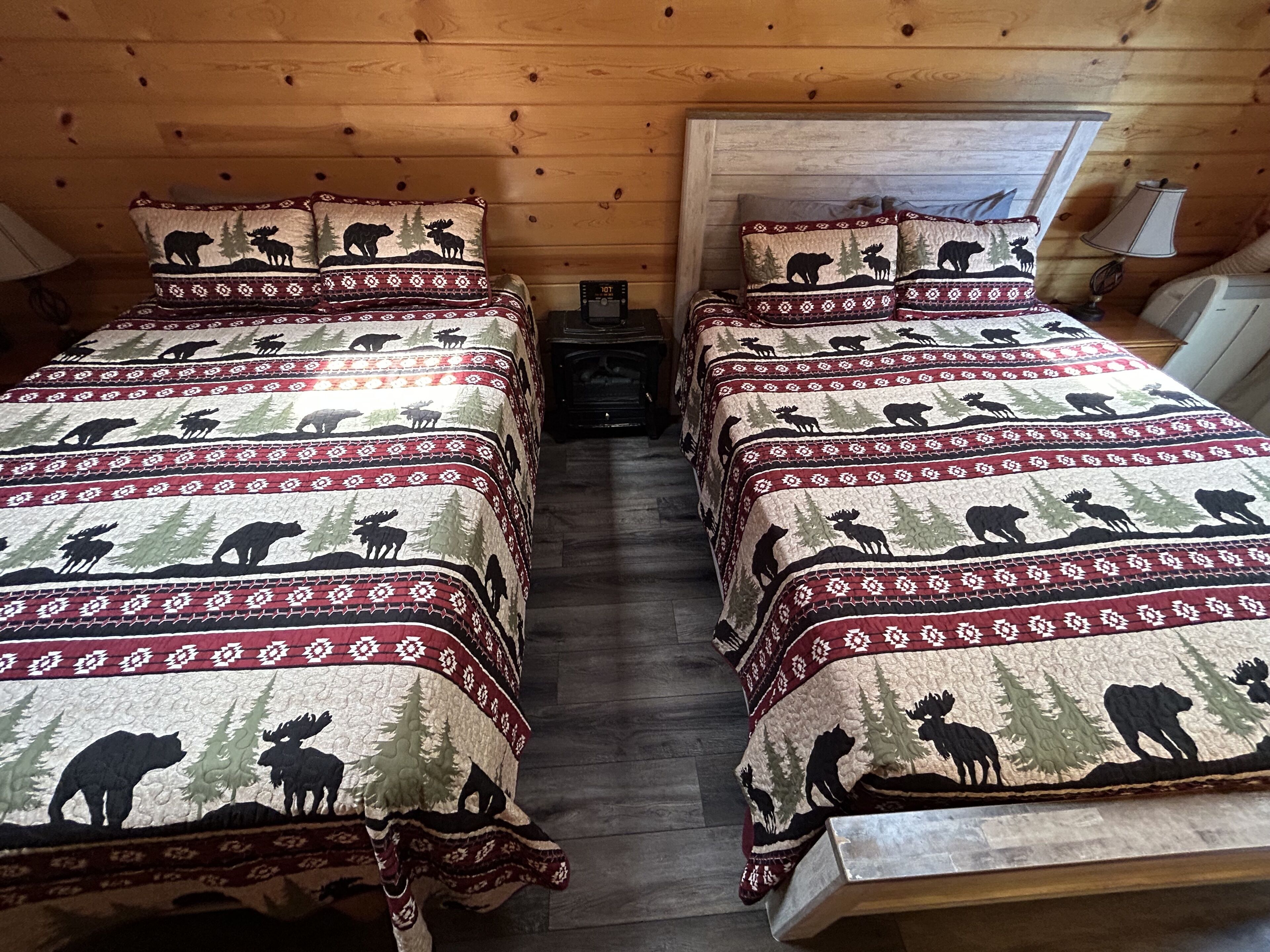 Una cabaña con dos camas, cada una con colcha acolchada que presenta siluetas de animales y un diseño rojo y blanco.