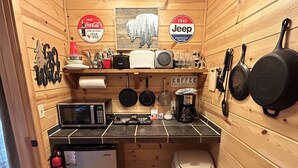 Eine kleine Küche mit Holzwänden, einer Mikrowelle, einer Kaffeemaschine und verschiedenen Küchenutensilien.