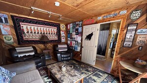 Ein gemütliches Zimmer mit einer Couch, einem Couchtisch und einer Tür zu einem weiteren Bereich. Die Wände sind mit verschiedenen Schildern und Postern dekoriert.