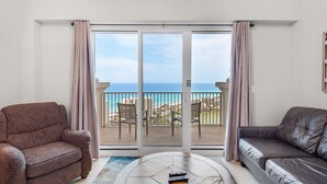 A living room with a large sliding glass door leading to a balcony with a view of the ocean. There are two sofas and a coffee table in the room.