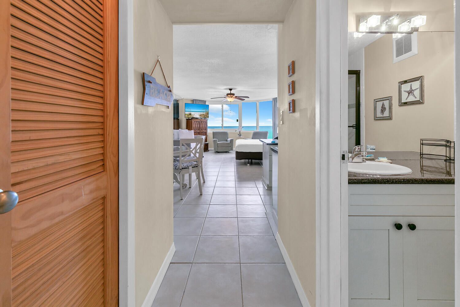 A hotel corridor with a wooden door, a dining area with a view, a bedroom, and a bathroom with a vanity.