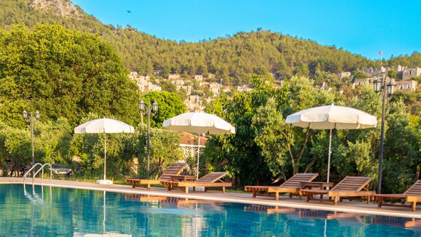 Una piscina con sillas de descanso y sombrillas, un frutero y una bebida en el borde.