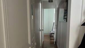 Un corridoio con pavimento in legno, pareti bianche e una porta a sinistra.