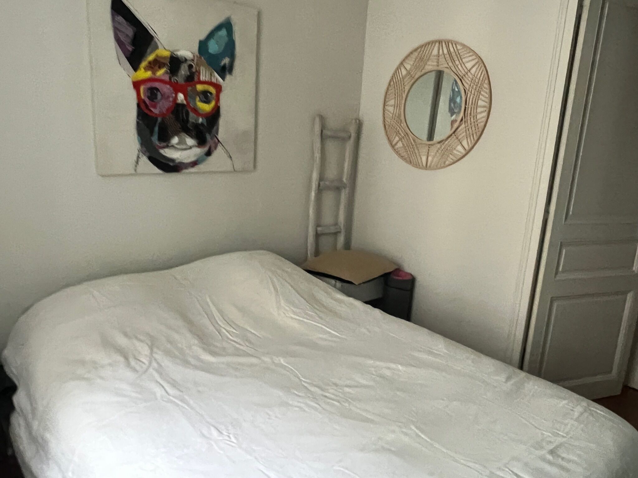 Quarto com cama branca, escada, espelho e pintura na parede.