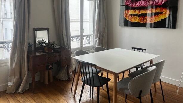 Un'area pranzo moderna con un tavolo e sedie bianche, un settimino in legno con specchio e un grande quadro floreale appeso al muro.