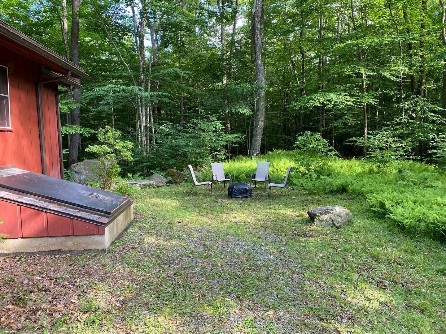 A cabin with a red exterior, a covered deck, and a small outdoor seating area with two chairs and a table.