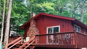 Une cabane rouge avec une cheminée en briques, un escalier en bois et une terrasse dotée de sièges d’extérieur.