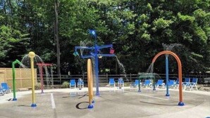Un espace de jeux aquatiques extérieur avec différents jets d’eau colorés et un coin salon équipé de chaises bleues.