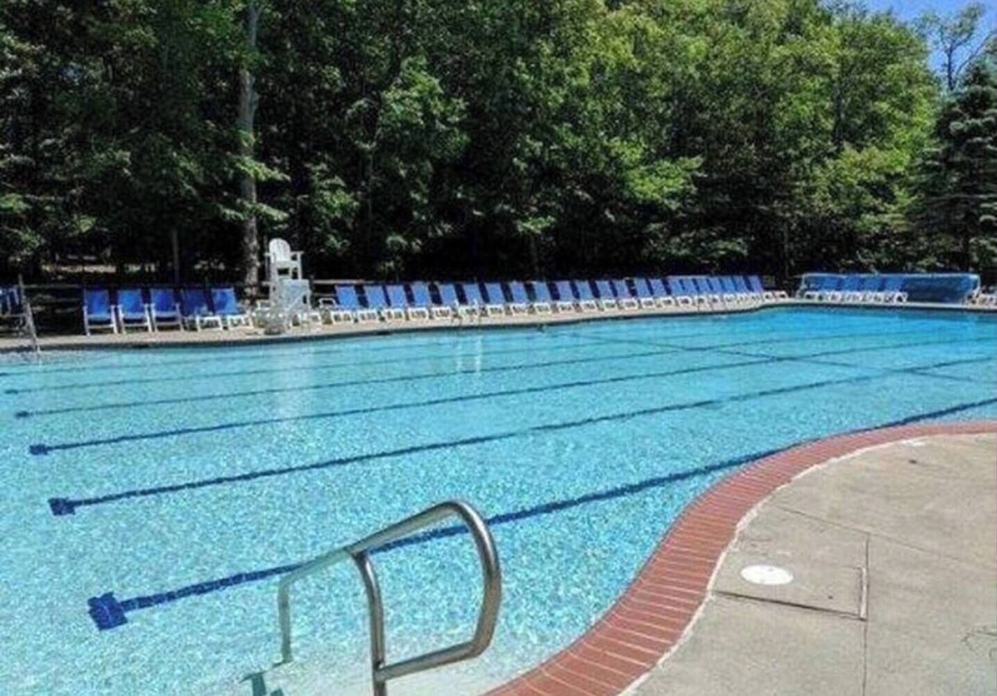 Ein Schwimmbecken mit Bahnen, umgeben von Bäumen und blauen Liegestühlen.