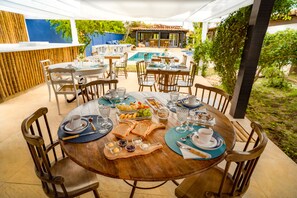 Un área de comedor al aire libre con mesas redondas, sillas y una piscina al fondo.