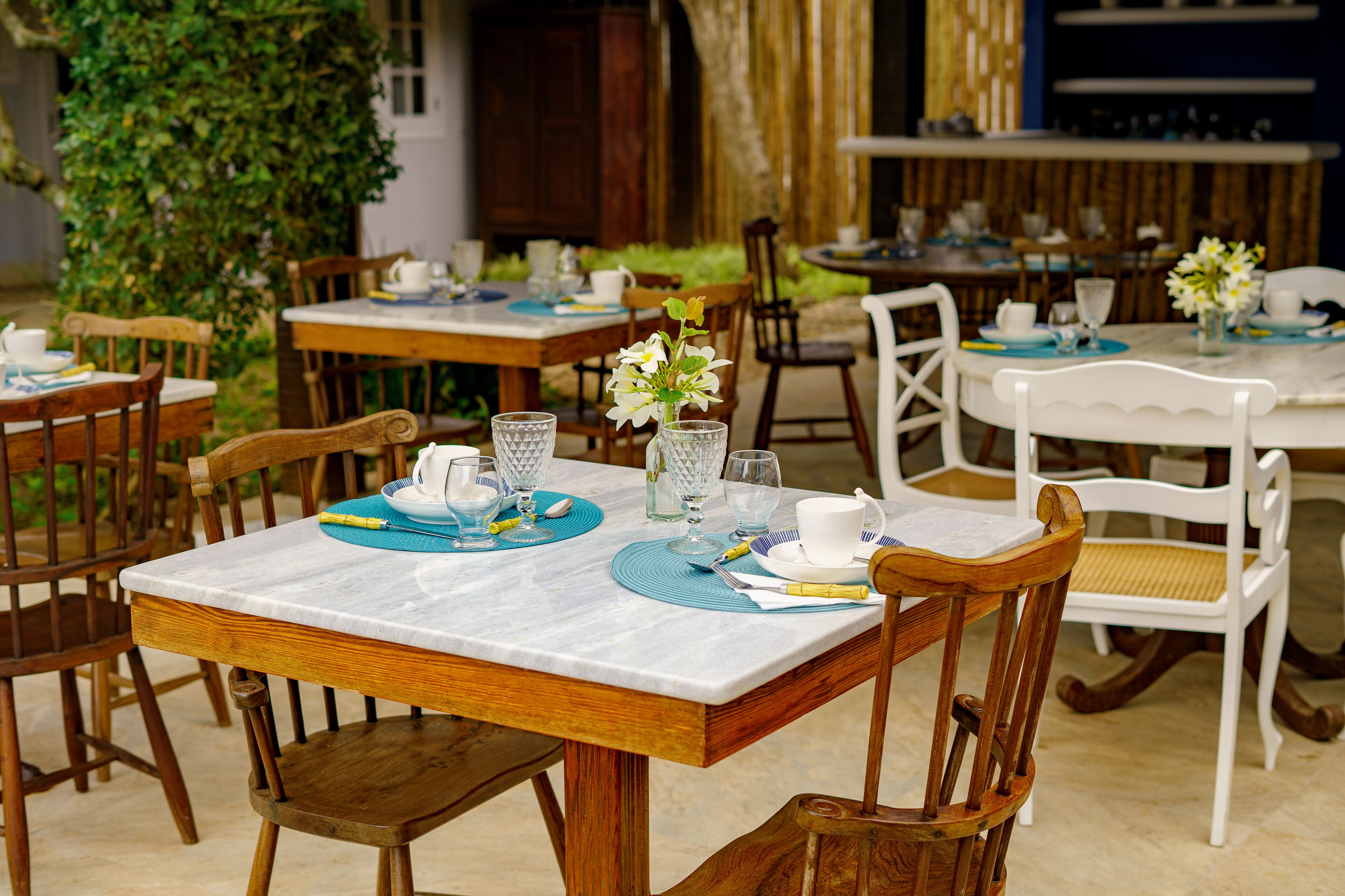 Un comedor con mesas y sillas de madera, algunas con manteles individuales azules y sábanas blancas.