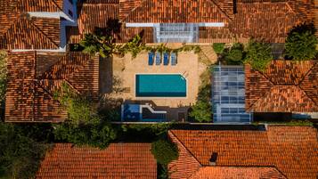An aerial view of a resort with a swimming pool, multiple villas with red-tiled roofs, and lush greenery.