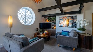 Een moderne woonkamer met een rond raam, een flatscreen televisie, een houten salontafel en twee grijze banken.