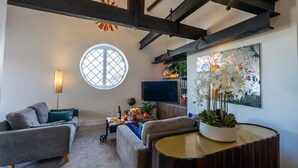Een moderne woonkamer met een groot raam, een ronde tafel met een potplant en een flatscreen tv aan de muur.