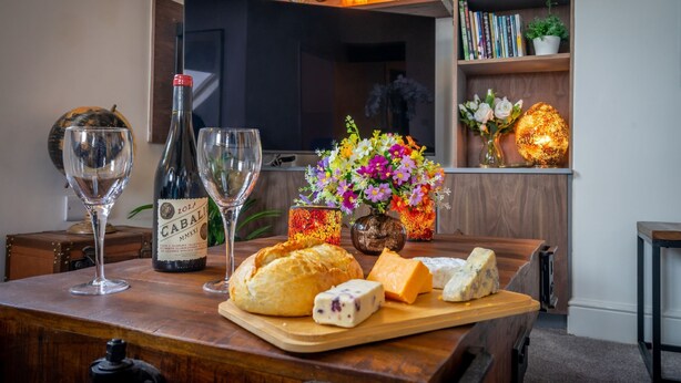 Een houten tafel met een fles Cabalier wijn, glazen, een brood en diverse kazen.