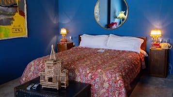Quarto com uma cama grande, um espelho, duas mesas de cabeceira com luminárias, uma mala e uma gaiola decorativa para pássaros.