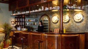 Zona de bar con armarios de madera, taburetes y estantes con varios objetos.