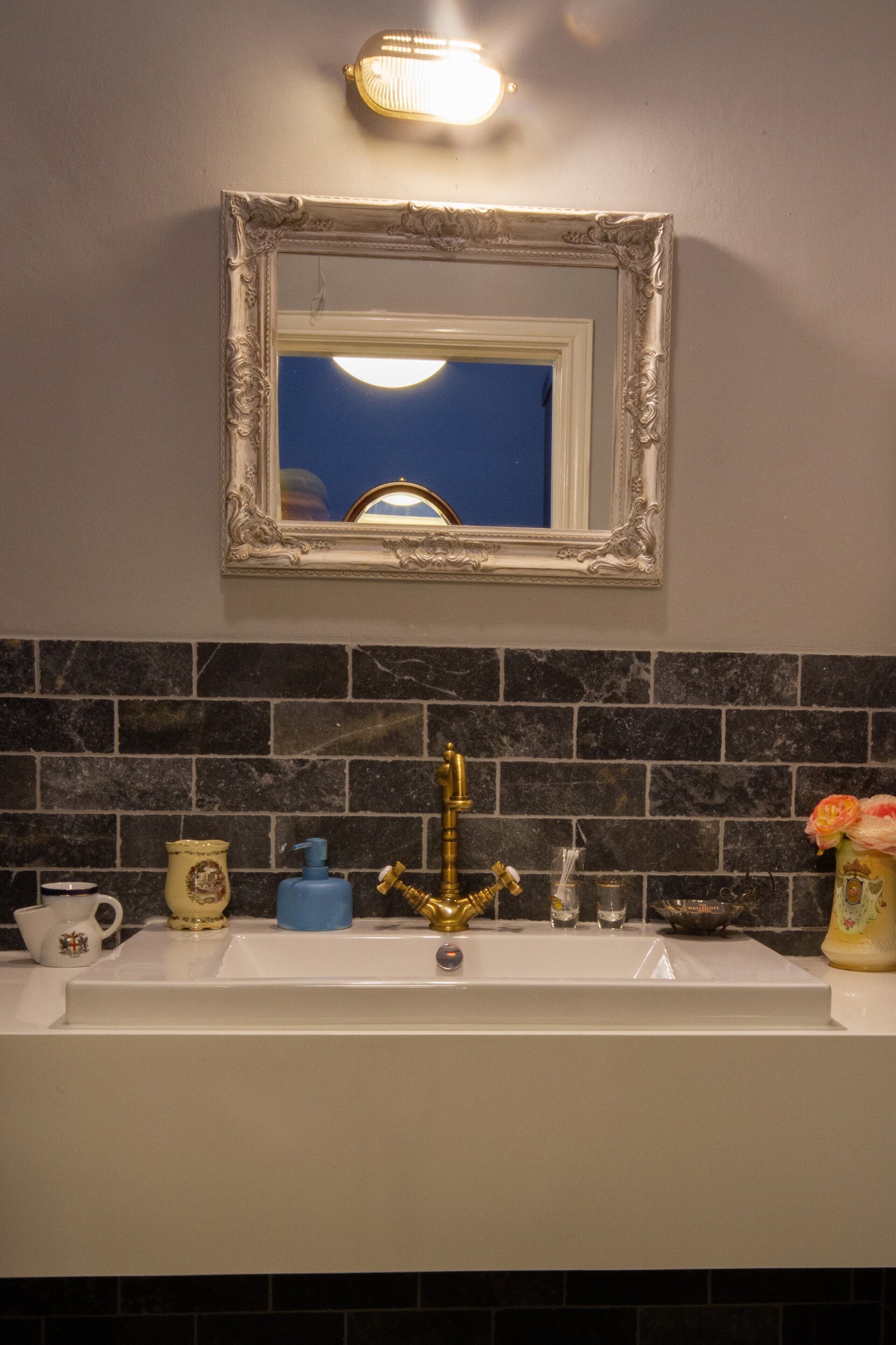 Un baño con un lavabo blanco, un grifo dorado y un espejo con un marco decorativo.