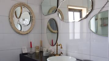 Un bagno con parete rivestita in piastrelle bianche, un piano d'appoggio nero, un lavandino bianco e diversi specchi con cornici decorate.