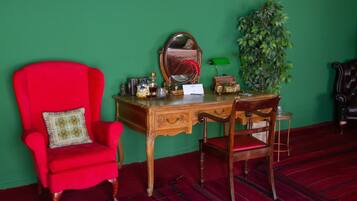 A room with a red armchair, a wooden desk with a mirror, a green wall, and a potted plant.