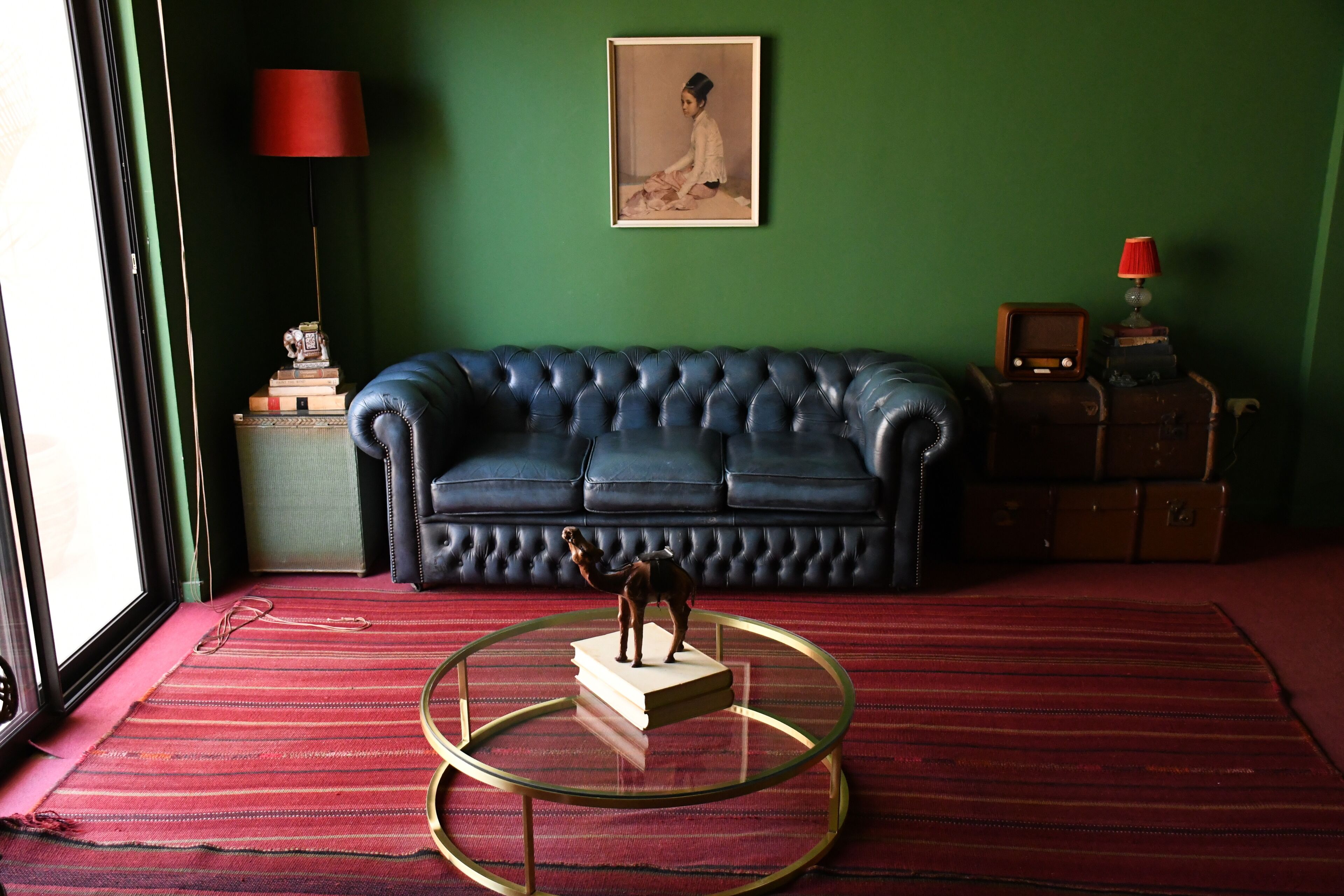 A room with a green wall, a blue sofa, a glass coffee table, a lamp, and a framed picture.