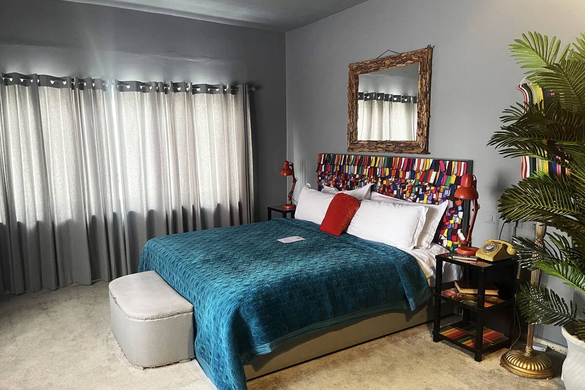 Quarto com cama, mesa de cabeceira, abajur, espelho e planta em vaso.
