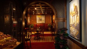 Un restaurante con alfombra roja, mesas y sillas de madera. Hay un cuadro grande en la pared y una presentación de alimentos a la izquierda.