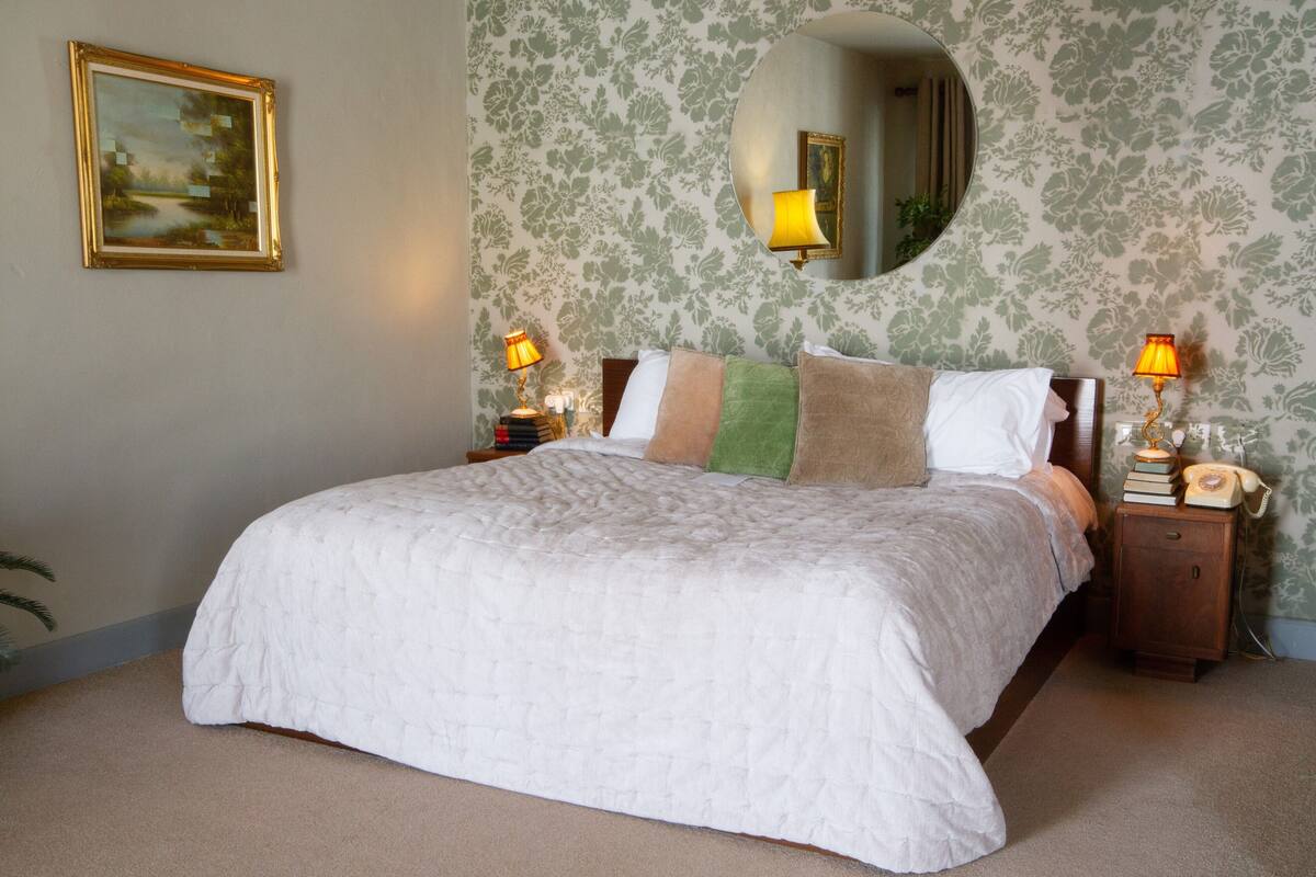 Uma cama bem arrumada com edredom branco acolchoado, cabeceira de madeira e duas luminárias de cabeceira.