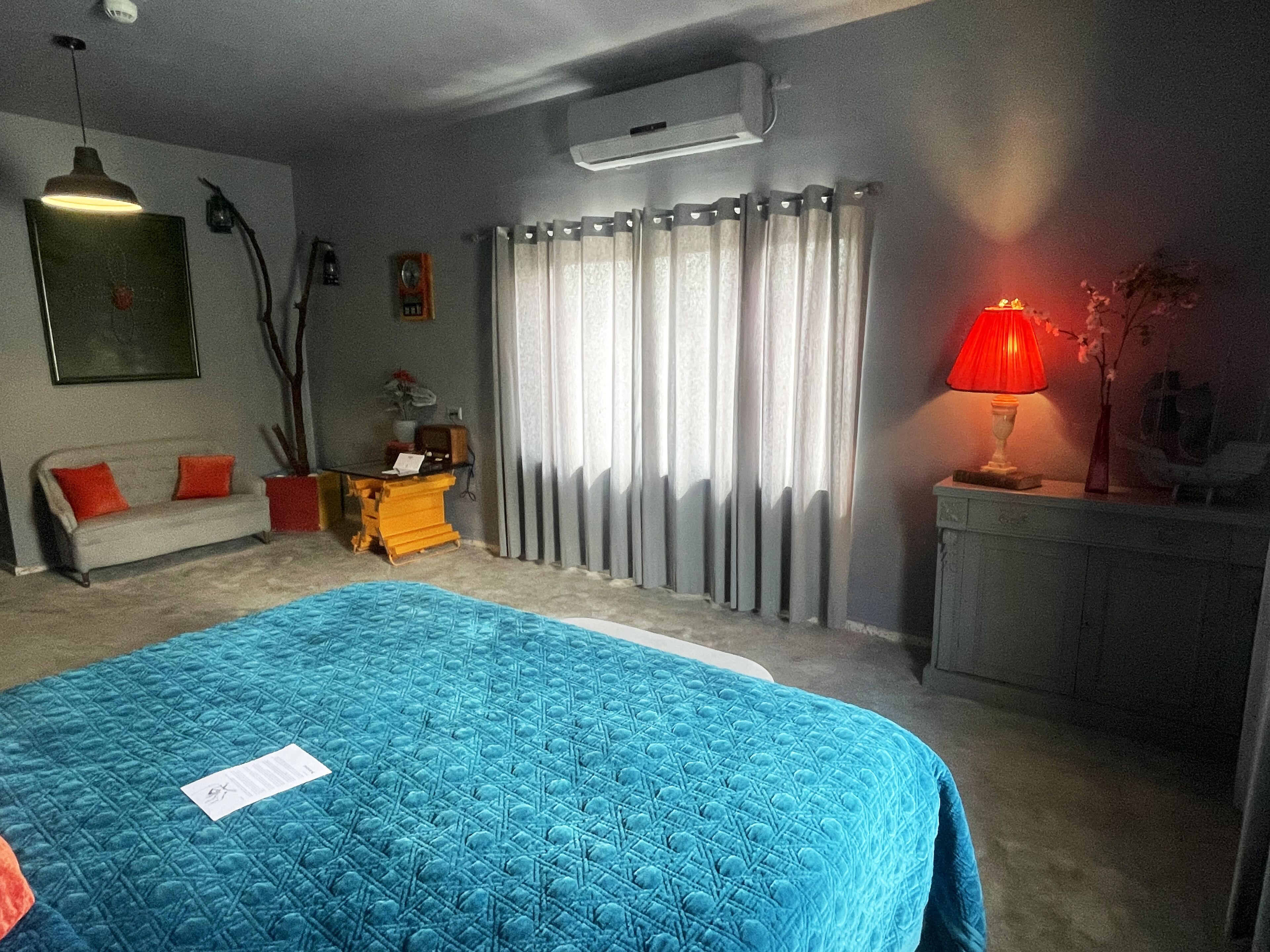 Ein Schlafzimmer mit einem großen Bett, einem Schreibtisch, einem Stuhl, einer Lampe und einem Fenster mit Vorhängen.