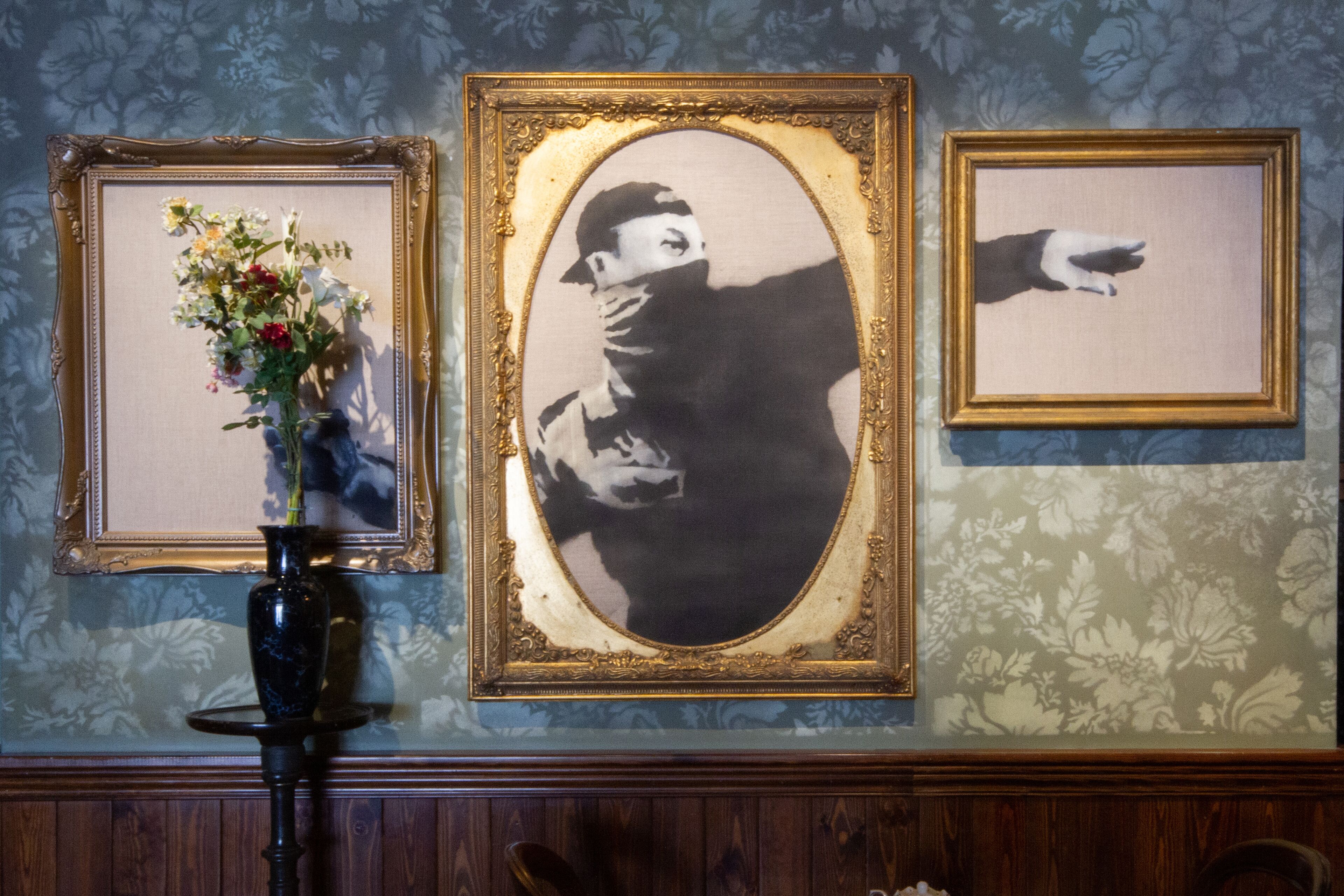 Three framed artworks on a wall with a floral wallpaper background.