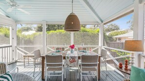 Een overdekt buitenontbijtgedeelte met een tafel voor vier personen, omringd door rieten stoelen, onder een hangende lamp.