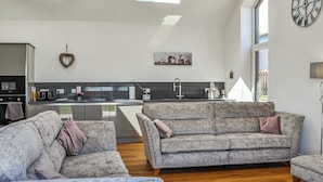 Un salon moderne avec un canapé gris et une table basse, une cuisine avec un pare-feu gris et une grande fenêtre qui laisse entrer la lumière naturelle.