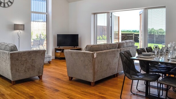 Un salon spacieux doté d’un grand téléviseur, de sièges confortables et d’un coin repas avec une table dressée pour six personnes.