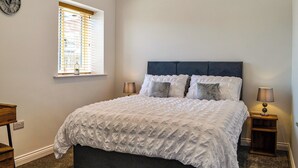 Une chambre à coucher comprenant un lit, deux tables de chevet, une fenêtre avec des stores, une horloge murale et un luminaire au plafond.
