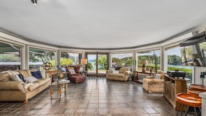 Ein großzügiger Wohnbereich mit gewölbter Decke, großen Fenstern mit herrlichem Ausblick und verschiedenen Sitzmöglichkeiten, darunter eine Couch, Sessel und ein Couchtisch.