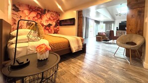 A modern hotel room with a bed, a round table with a lamp, a chair, and a large floral wall mural.