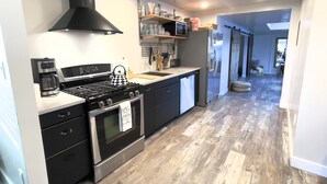A modern kitchen with a gas stove, oven, and dishwasher, a black range hood, and a wooden floor.