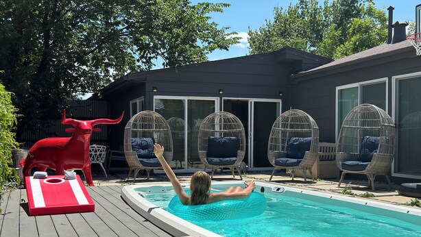 A swimming pool with a person relaxing, surrounded by wicker chairs and a red bull statue.