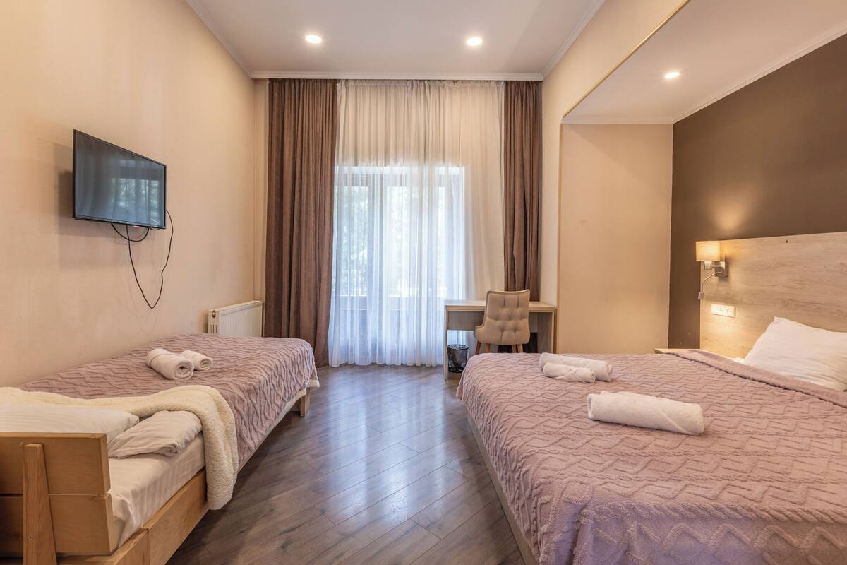 A hotel room with two beds, a desk, a chair, a television, and a window with curtains.