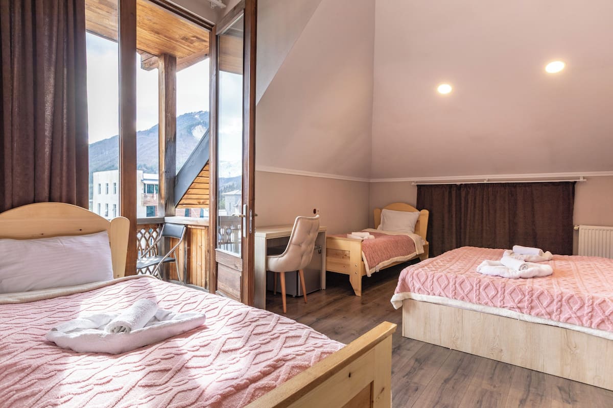 A hotel room with two beds, a desk, a chair, and a view of mountains.