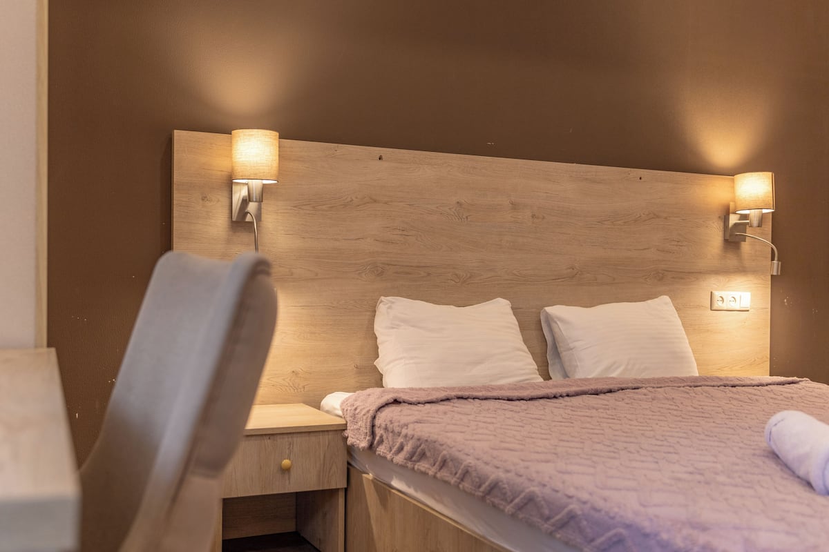 A bedroom with a wooden headboard, two bedside lamps, a bed with white linens, and a chair.