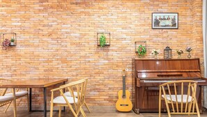 Una habitación con pared de ladrillo, un piano de madera, una guitarra y una mesa de comedor con sillas.