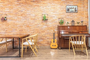 Ein Zimmer mit Backsteinwand, einem Holzklavier, einer Gitarre und einem Esstisch mit Stühlen.