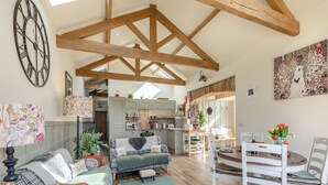 A spacious living room with a high ceiling, wooden beams, a large clock, and a cozy seating area with a table and chairs.