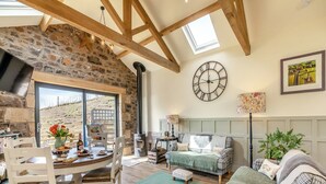 A cozy living room with a stone wall, wooden beams, a large clock, and a view of the outdoors.