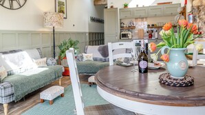 A cozy living room with a wooden ceiling, a round table with a vase of flowers, and a clock on the wall.