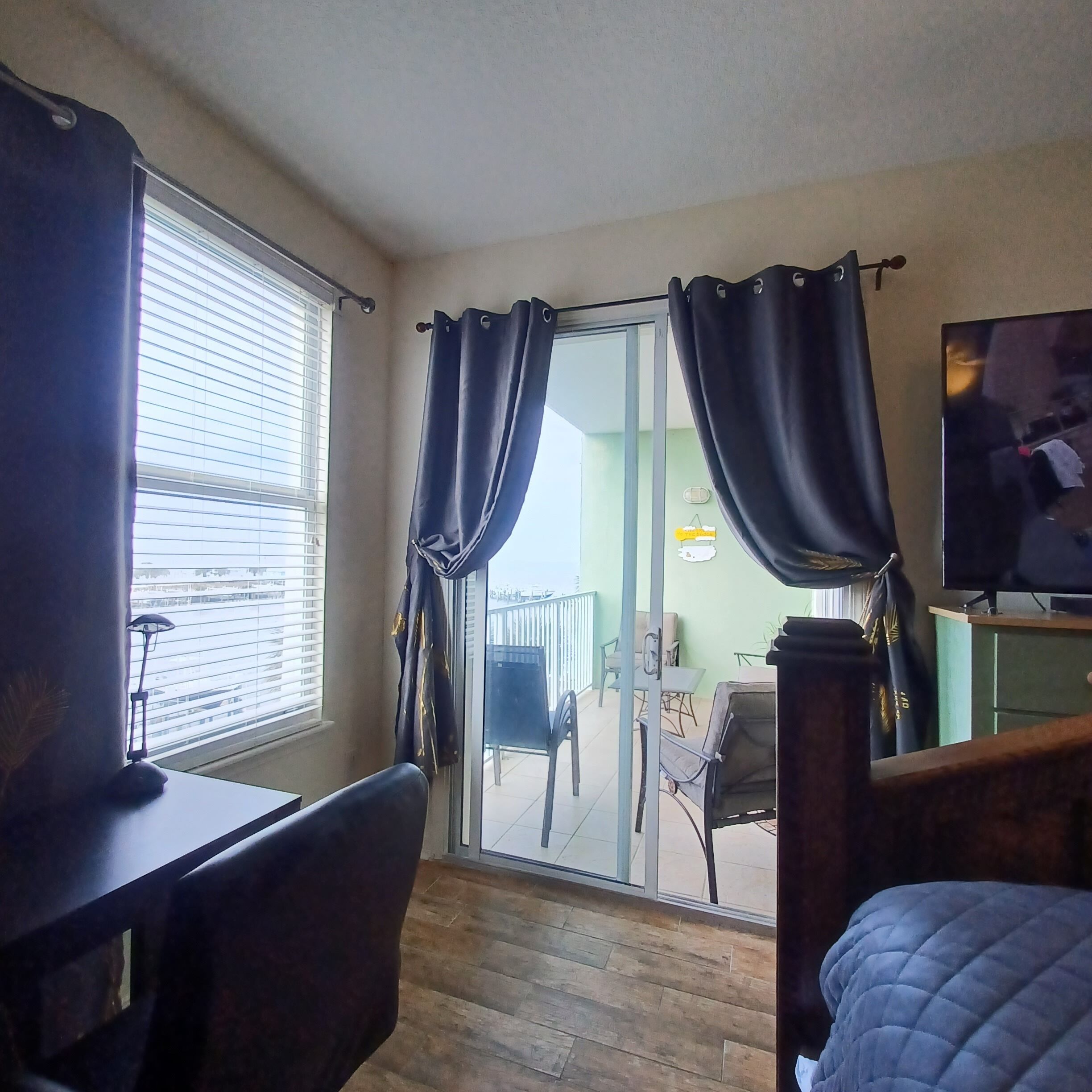 A hotel room with a bed, a desk, a chair, a TV, and a sliding glass door leading to an outdoor area with a table and chairs.