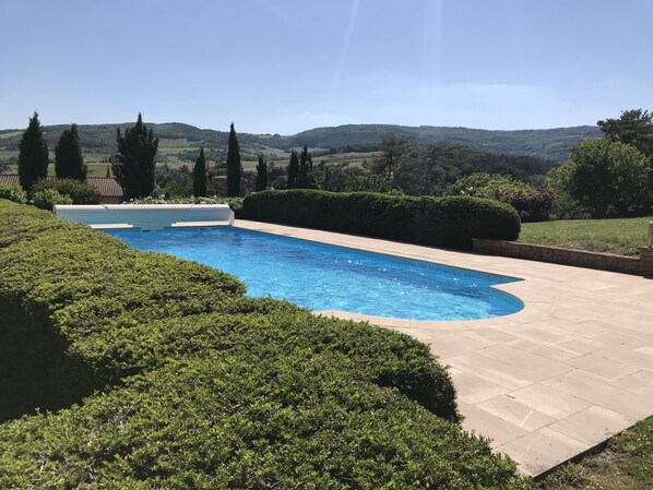 Une piscine rectangulaire à l’eau d’un bleu limpide, entourée de haies bien entretenues et d’une terrasse dallée.