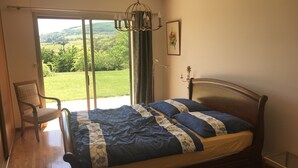 Une chambre avec un lit en bois, une chaise, une vue sur la verdure grâce à une porte coulissante et un lustre.